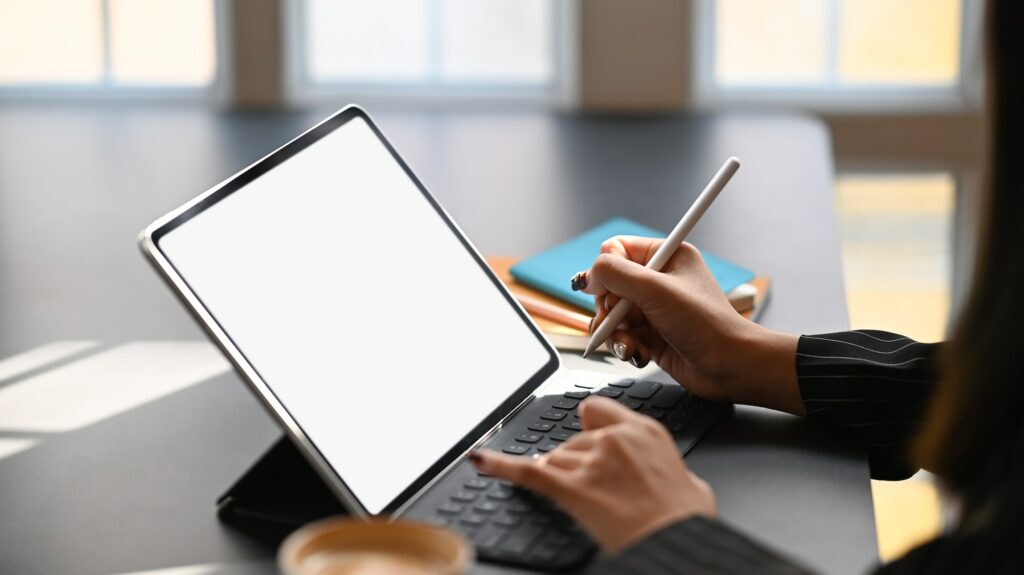 Cropped shot of business woman typing on keyboard of tablet and holding electric pen.